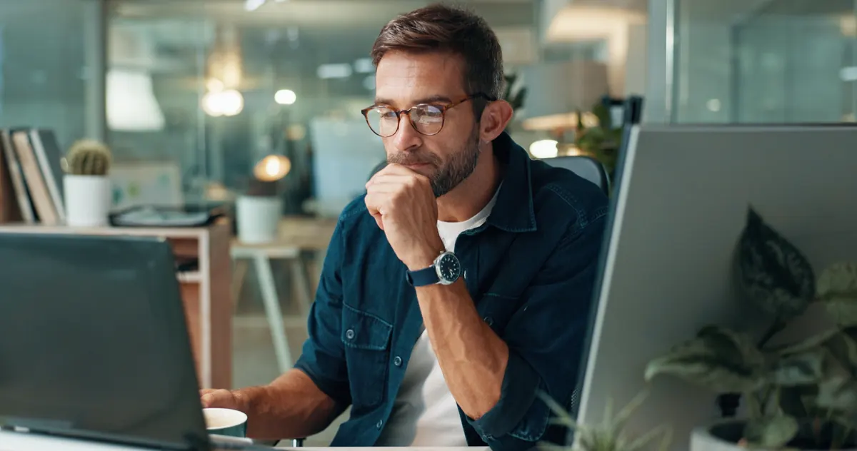 A person studying figures on a monitor, chin resting on one hand.